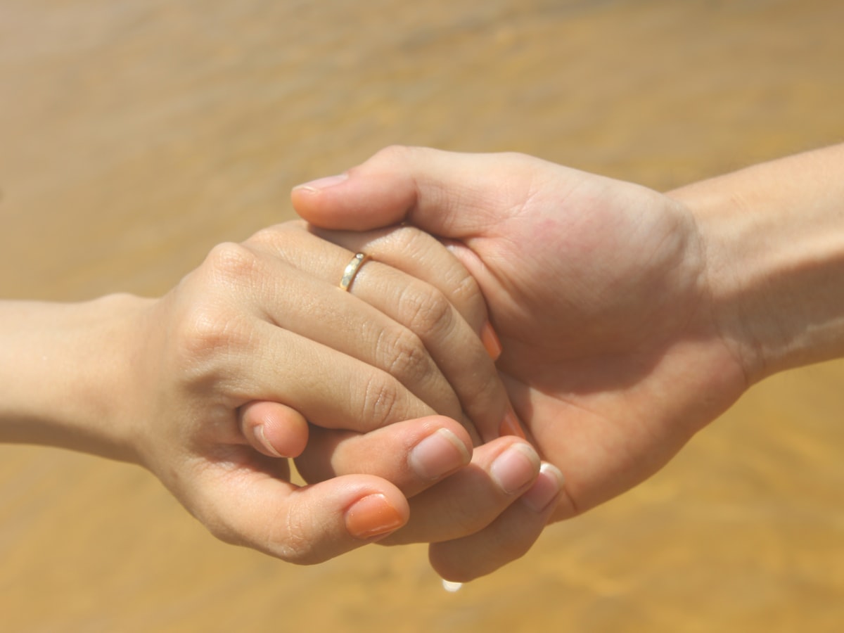 Two partners holding hands, one wearing a ring, in warm daylight